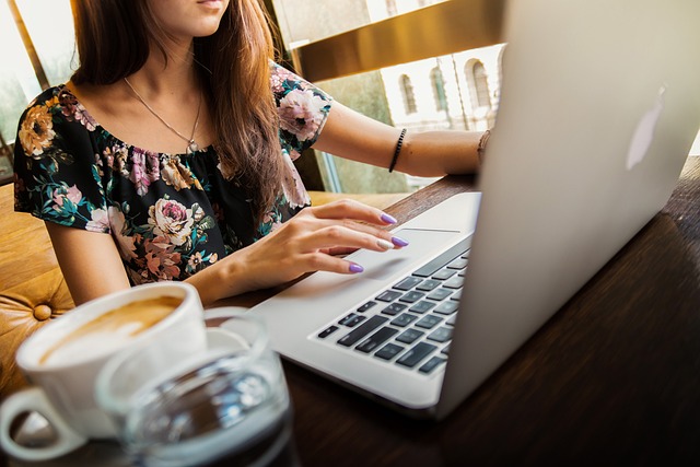 A woman sitting at a desk working on a laptop computer with a coffee mug next to it.